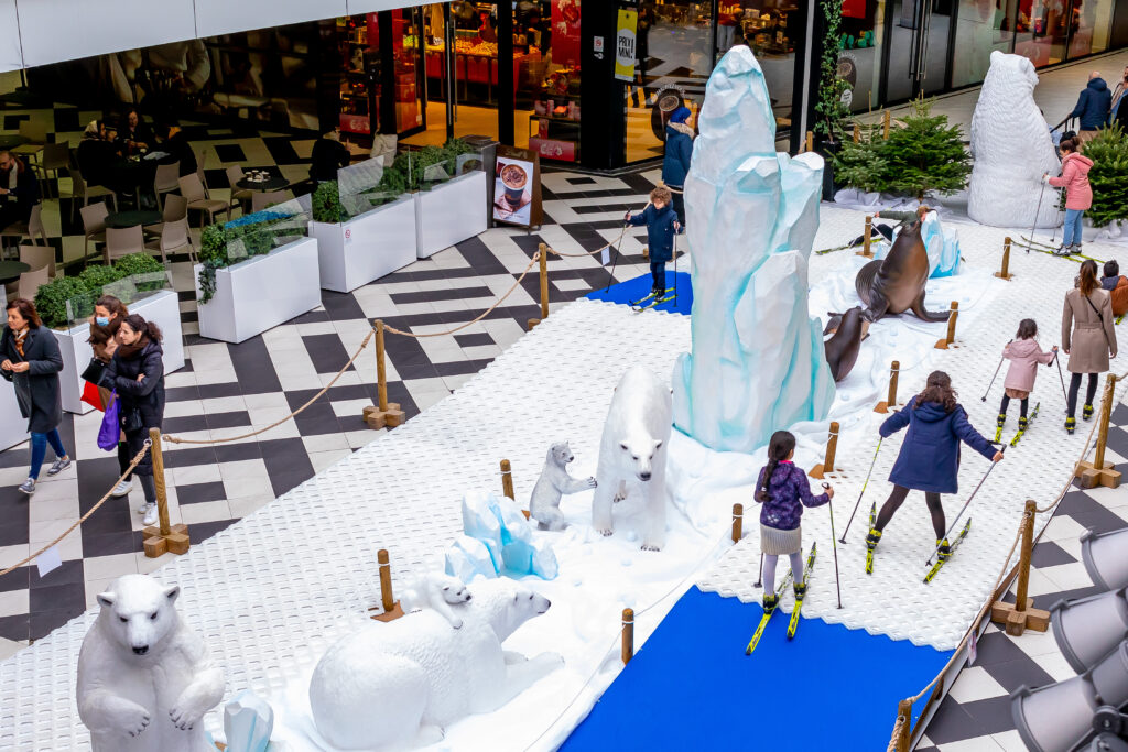 Enfants sur une piste de ski de fond synthétique dans une galerie marchande avec décor de banquise