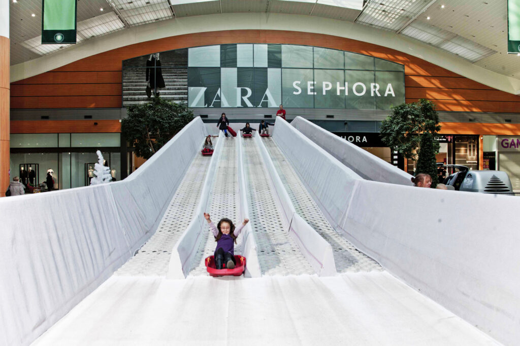 Enfant en bouée rouge dévalant une piste de luge synthétique dans une galerie marchande