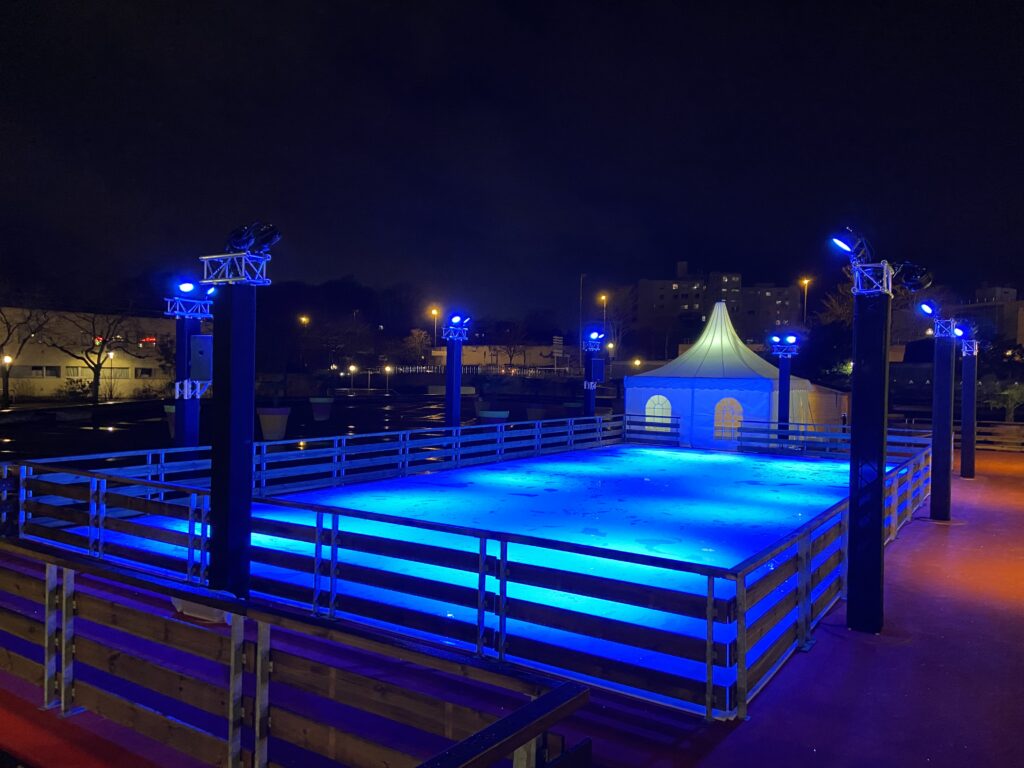 Patinoire synthétique sous un chapiteau éclairé en bleu la nuit