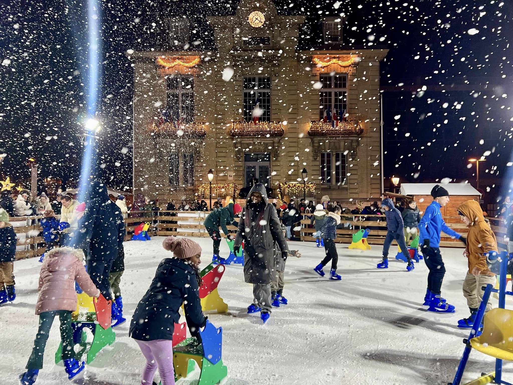 Neige artificielle sur la patinoire devant une façade illuminée