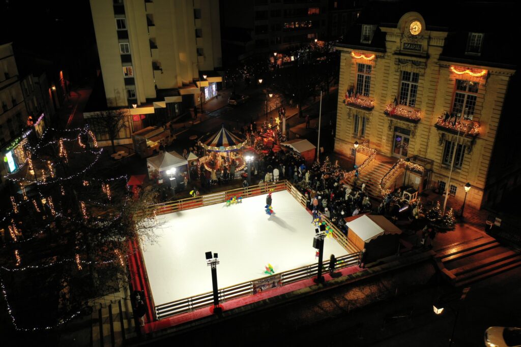 Vue aérienne d’une patinoire synthétique sur une place avec marché de Noël de nuit